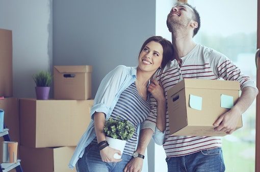 A smiling couple holding moving boxes and a plant, an example of renters working with United Properties' West Michigan property management