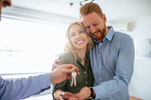 A smiling couple accepts a set of keys in their hand, an example of renters working with United Properties' West Michigan property management